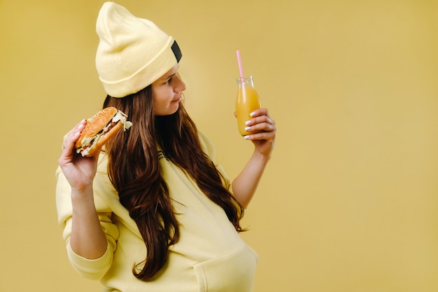 Zwanger meisje in gele kleren met hamburgers in haar handen op een gele achtergrond