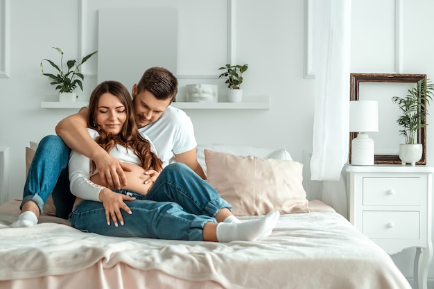 Zwanger meisje met haar echtgenoot ligt op het bed. Mooie buik van een jong aantrekkelijk zwanger meisje. Familie, huwelijk, bevalling concept.