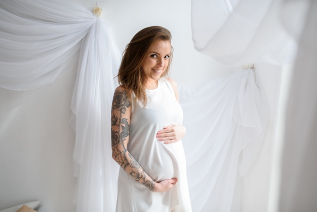 Zwanger meisje met tatoeage in een witte jurk.