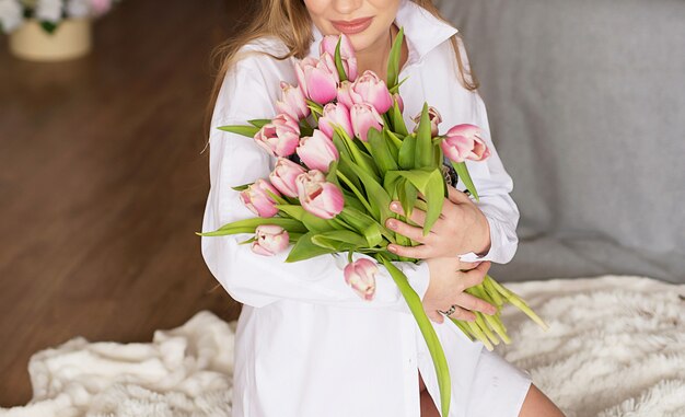 Zwanger meisje op een lichte achtergrond met bloemen. Foto zonder gezicht in het kader.