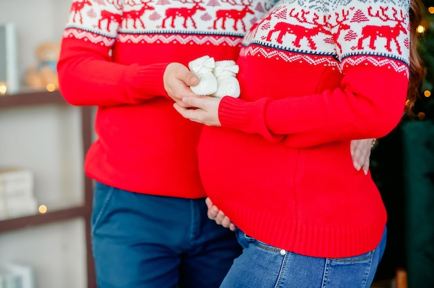 Foto zwanger stel in identieke nieuwjaarssweaters die buik aanraken op kerstvakantie voor nieuwjaar