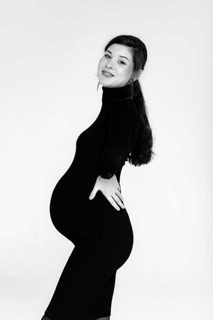 Zwangere brunette in een zwarte jurk met een nek op een witte achtergrond