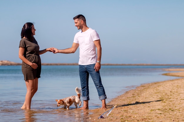 Zwangere gelukkige paar met kleine hond op strand