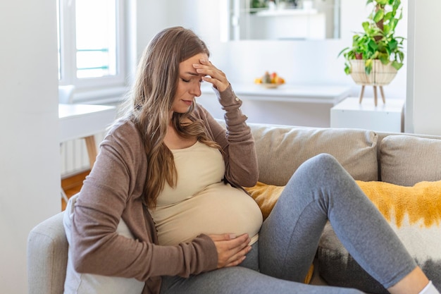 Zwangere jonge volwassen vrouw die thuis op de bank rust en zich onwel voelt Jonge zwangere vrouw ziek