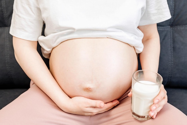 Zwangere jonge vrouw die melk drinkt terwijl ze thuis op de bank zit