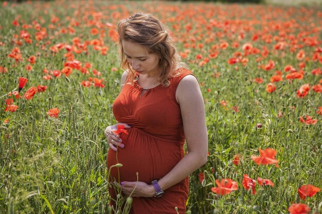 Zwangere jonge vrouw die te midden van bloemen op het land staat