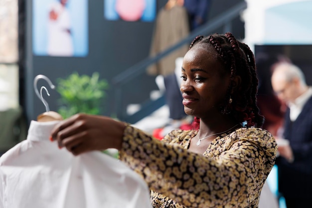 Zwangere klant die trendy wit overhemd controleert in moderne boetiek, winkelen voor modieuze zwangerschapskleding. Afro-Amerikaanse vrouw die stijlvolle formele kleding koopt in een kledingwinkel. Mode-concept
