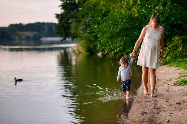 Zwangere moeder die met haar zoontje in de zomerpark dichtbij het meer loopt