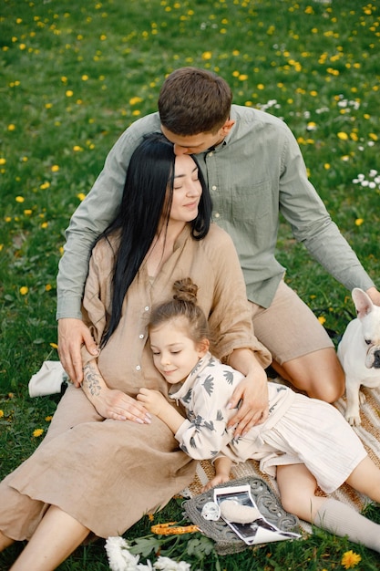 Zwangere moeder en haar dochtertje en echtgenoot zittend op een gras in een park