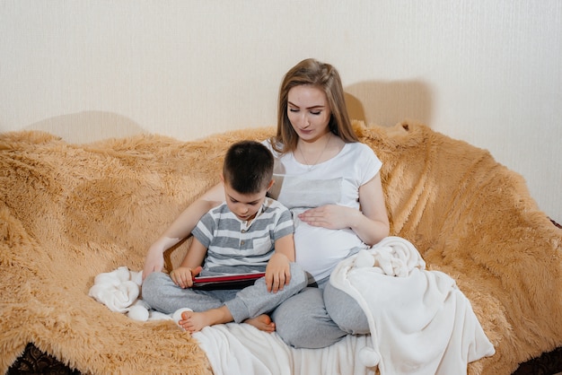 Zwangere moeder speelt met haar zoon op de bank in de tablet. Zorg, familie, liefde