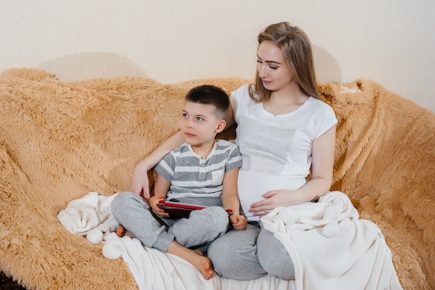 Zwangere moeder speelt met haar zoon op de bank in de tablet. zorg, familie, liefde.