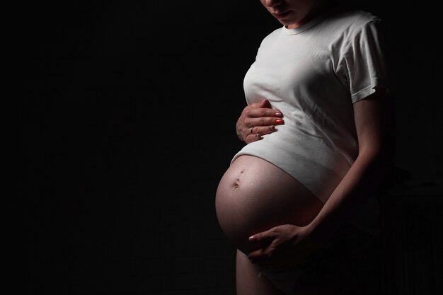 Zwangere mooie jonge vrouw in witte t-shirt knuffels buik met baby