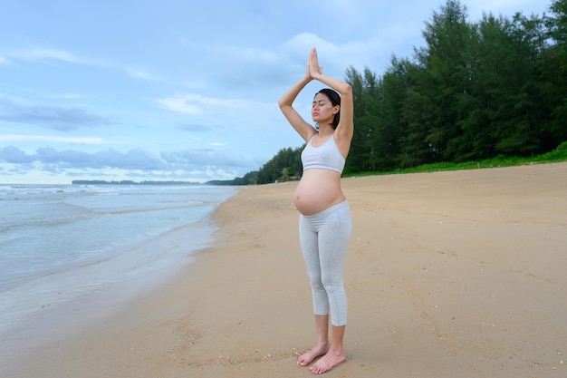 Zwangere vrouw beoefent yoga en meditatie terwijl ze boomhouding doet op rustig strand met natuurtafereel Gezond levensstijlconcept