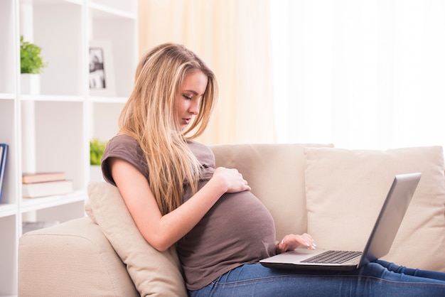 Zwangere vrouw die aan laptop werkt terwijl het liggen op een laag.