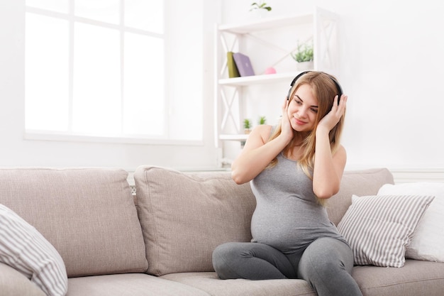 Zwangere vrouw die aan muziek in hoofdtelefoons luistert. Jonge aanstaande blonde genieten van klassieke melodie, kopieer ruimte. Ontspan, vrije tijd, zwangerschapsconcept