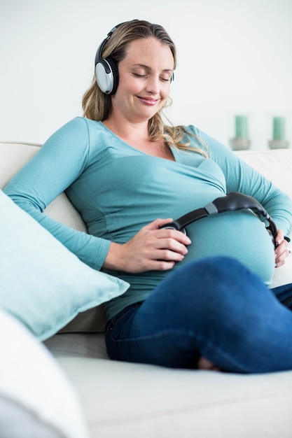 Zwangere vrouw die aan muziek met hoofdtelefoons op buik op de laag luistert