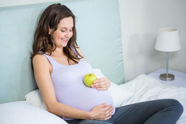 Zwangere vrouw die een appel op haar buil houdt liggend in haar bed