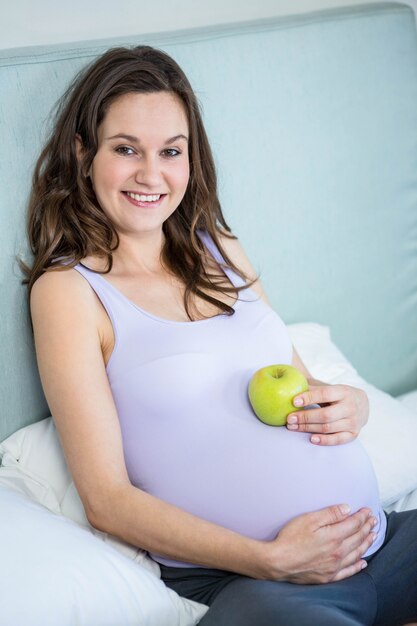 Zwangere vrouw die een appel op haar buil houdt liggend in haar bed