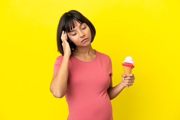 Zwangere vrouw die een cornetroomijs houdt dat op gele achtergrond met hoofdpijn wordt geïsoleerd