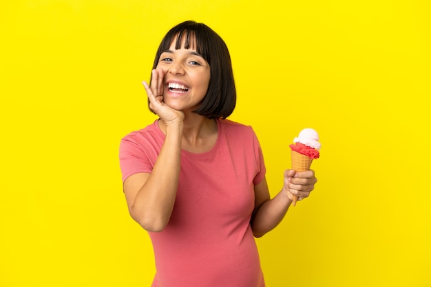 Zwangere vrouw die een cornetroomijs houdt dat op gele achtergrond wordt geïsoleerd en met wijd open mond schreeuwt