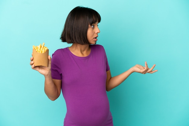 Zwangere vrouw die gefrituurde chips over een geïsoleerde achtergrond vasthoudt met een verbaasde uitdrukking terwijl ze opzij kijkt