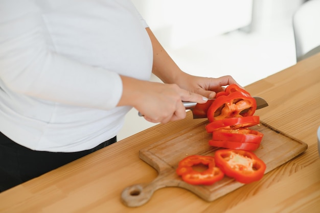 Zwangere vrouw die groenten thuis in de keuken snijdt