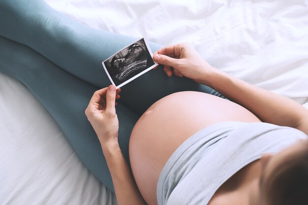 Zwangere vrouw die haar buik aanraakt en naar echografie in bed kijkt