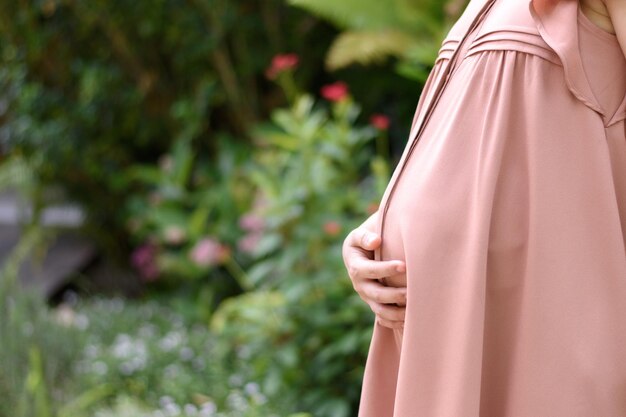 Foto zwangere vrouw die haar buik omhelst en vasthoudt in de tuin