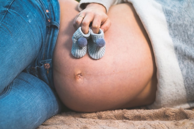 Zwangere vrouw die in openlucht het houden van weinig babyschoenen op haar buik stelt.