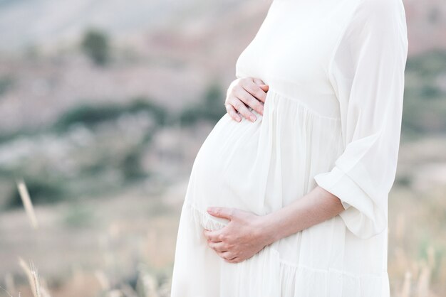 Zwangere vrouw die jurk draagt die buiten over de natuur poseert