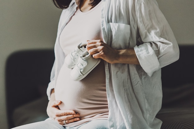 Zwangere vrouw die kleine babyslofjes houdt. levensstijl. moederschap concept.