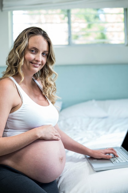 Zwangere vrouw die laptop op haar bed met behulp van