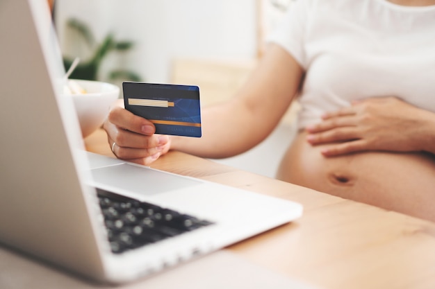 Zwangere vrouw die online thuis het winkelen op laptop maken