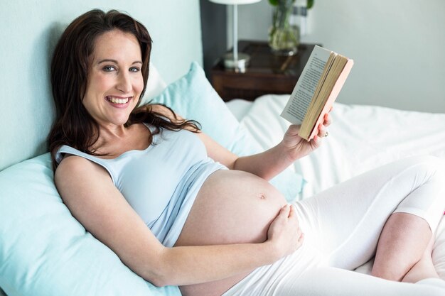 Zwangere vrouw die op bed een boek thuis leest