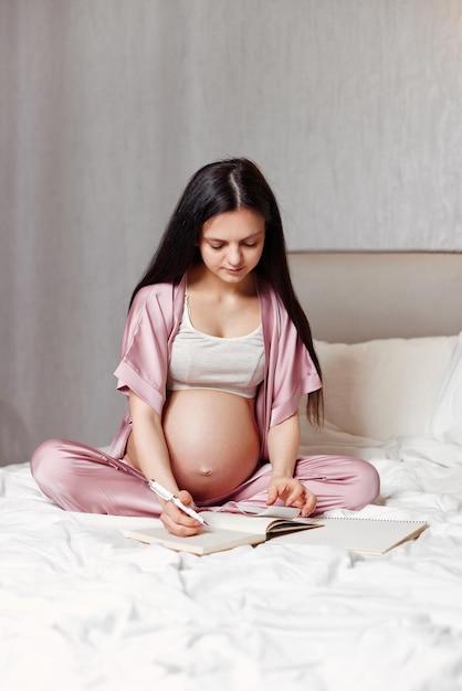 Zwangere vrouw die op bed zit en in notitieboekje schrijft