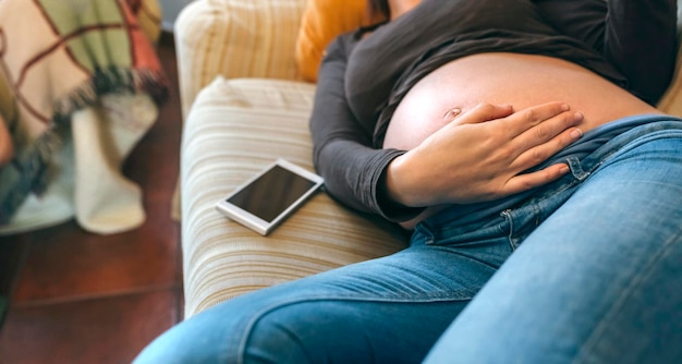 Foto zwangere vrouw die op de bank ligt en haar buik streelt in de woonkamer