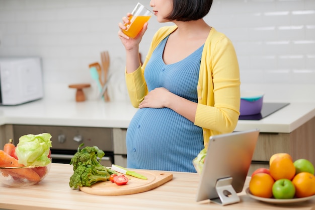 Zwangere vrouw die op keuken gezond vruchtensap drinkt