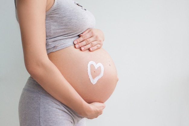 Foto zwangere vrouw die rood hart en hand op haar buik houden, symbool van het nieuwe leven, concept het verwachten voor baby en het uitbreiden van familie