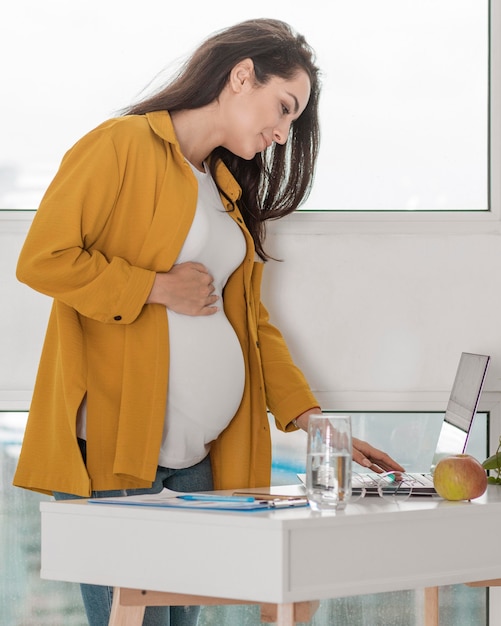 Foto zwangere vrouw die thuis aan laptop werkt