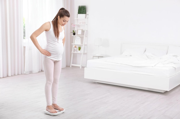 Zwangere vrouw die thuis op een weegschaal staat Zwangerschapsgewichtstoename concept