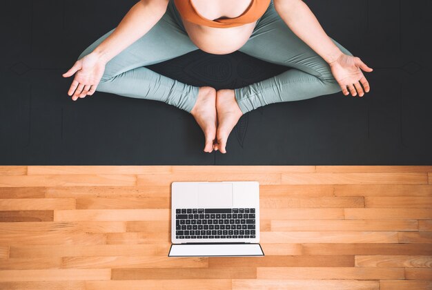 Zwangere vrouw die thuis yoga beoefent met laptop Vrouwelijke oefening mediteert tijdens de zwangerschap