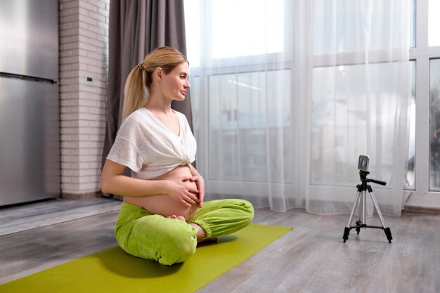 Zwangere vrouw die thuis yoga beoefent met smartphone aanstaande moeder die prenatale videotraining doet