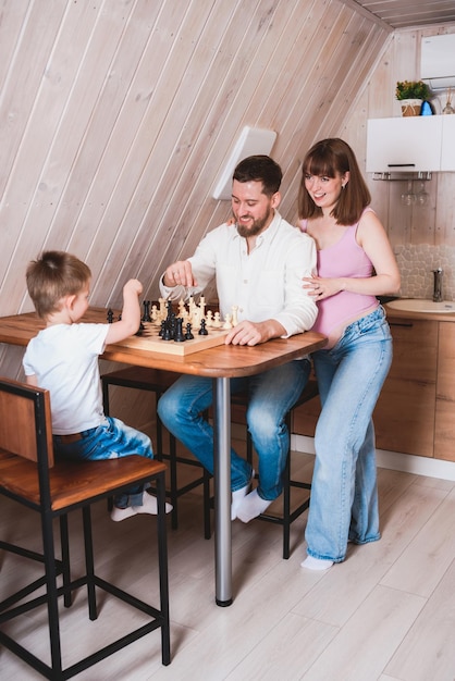 Zwangere vrouw die vader en zoon aan tafel ziet schaken