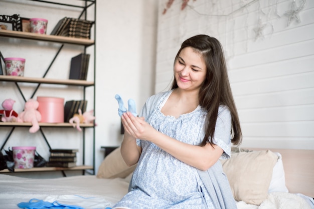 Zwangere vrouw die van babykleren kijkt. Jonge moeder die van een baby wacht.