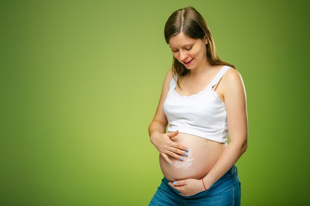 Zwangere vrouw die voor de buikhuid zorgt en een speciale vochtinbrengende crème gebruikt tegen rekken