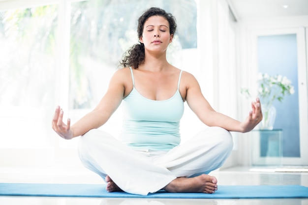 Zwangere vrouw die yoga met ogen doet die op oefeningsmat worden gesloten