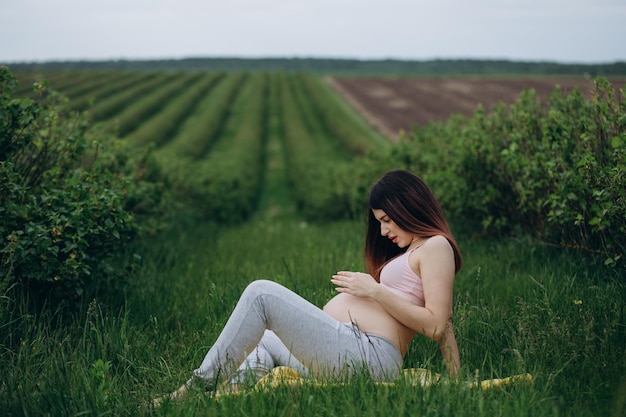 Zwangere vrouw doet fitness oefening op het gras in zonnige zomerdag