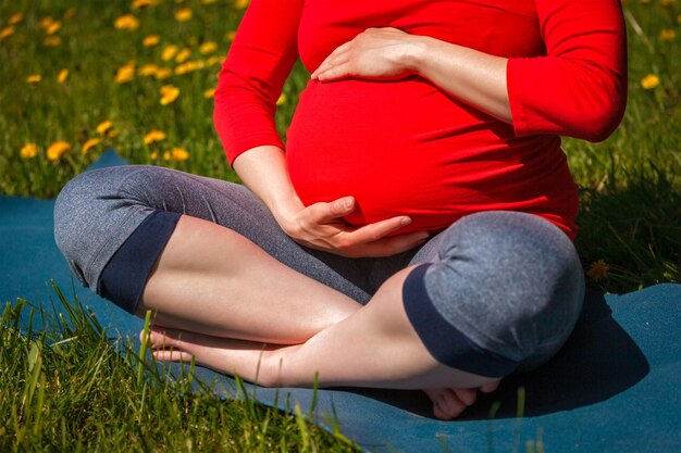 Zwangere vrouw doet yoga asana Sukhasana in de buitenlucht