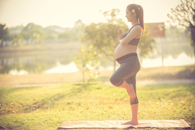 Zwangere vrouw doet yoga op het veld.