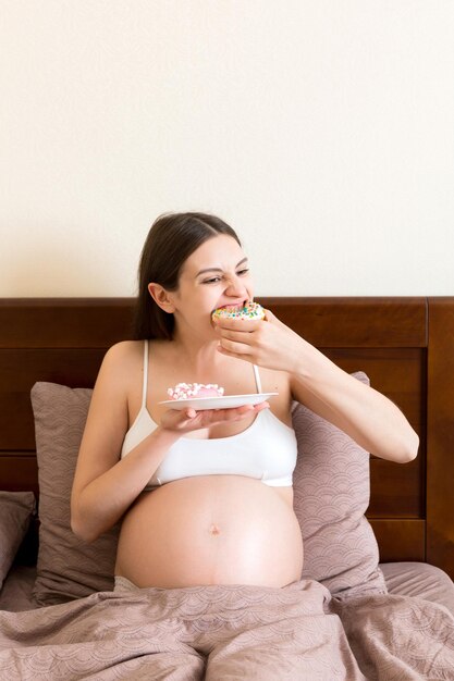 Zwangere vrouw eet veel donuts ontspannen in bed ongezond dieet tijdens zwangerschap concept